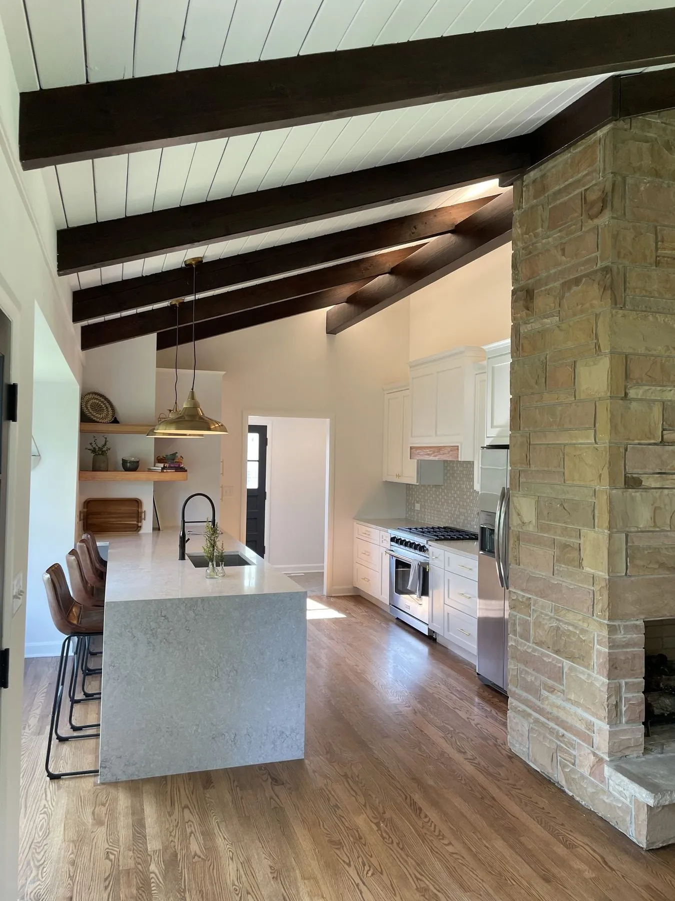 Kitchen with dark ceiling beams, a waterfall island, and a stone fireplace