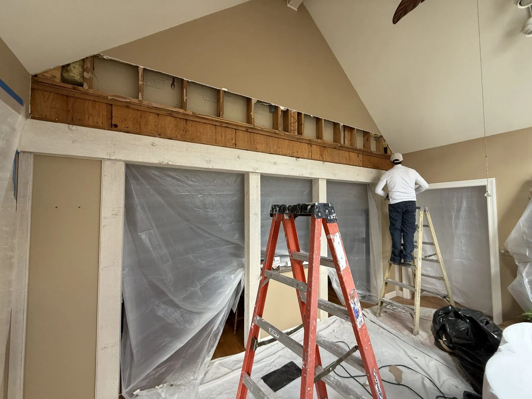 Framing work underway in a vaulted room, with plastic dust barriers up