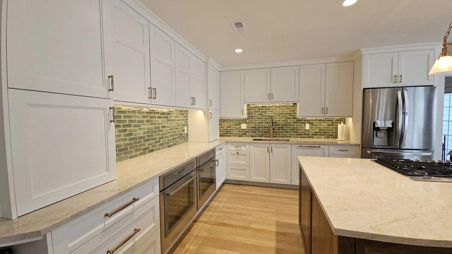 Wall of white cabinets and green tile backsplash beside a stainless refrigerator